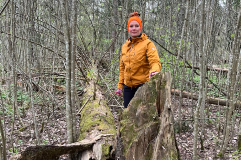 Pirkko Väkimies seisoo lahopuun vieressä metsässä